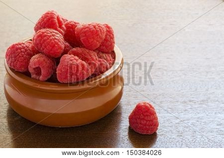 Fresh raspberries in a clay bowl on wooden background