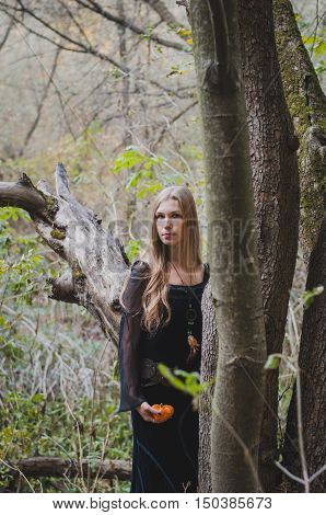 Blond long-haired girl in a fantasy black dress in an autumn forest scary halloween fairy tale