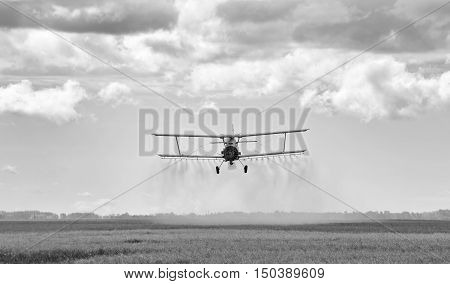 Spray plane swooping down and spraying chemical on a agriculture field at harvest in black and white