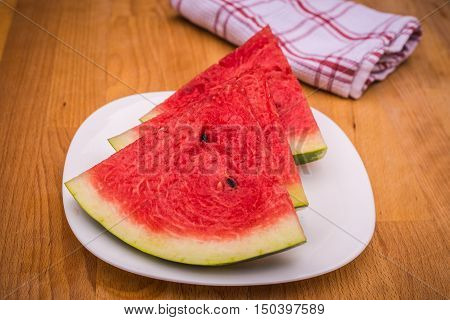 Watermelon slices on the white porcelain plate served with napkin straw-coloured wooden background
