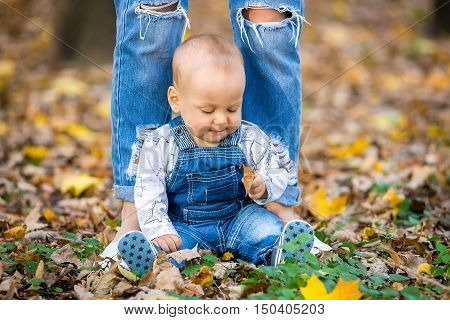 Happy happy baby sitting in the park with yellow leaves in autumn. In autumn park kid sitting in yellow leaves. Cheerful baby sitting in the park. Warm autumn day in the park.