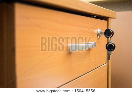 Closed drawer of his desk with the keys in the lock