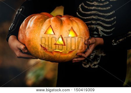 Hands Boy in halloween masquerade costume ih light from pumpkin head. Close-up