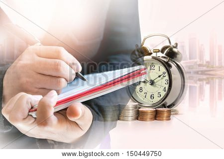 Double exposure of businesswoman take notes on the book with a row of stack money coins and analog clock on the blurred cityscape background concept for business finances and saving money.