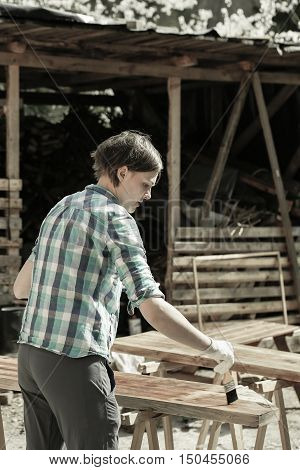 Woman applying and protecting garden furniture with fresh wood treatment paint. Outdoor protection carpentry hard at work home improvement do-it-yourself concept.