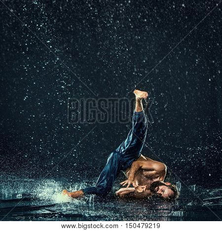 The male break dancer in water on dark background.