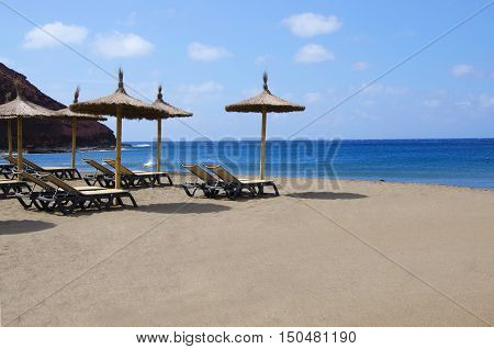 Sunbeds and umbrella a beautiful beach de MedanoTenerife Canary Islands. Concept for vacations or tourism with copyspace.