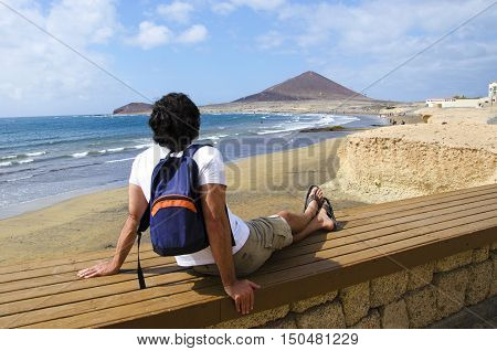 Young man with backpack looking on the sea and mountain. Rear view photo