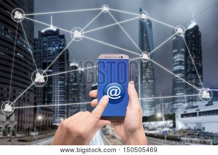 Hand holding smartphone and click on button with at sign linked with people icons. Email marketing newsletter and bulk mail concepts.