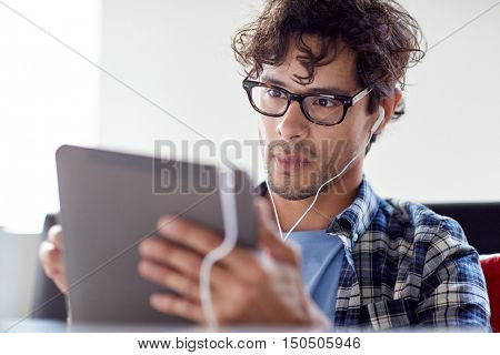 leisure, technology, communication and people concept - creative man with tablet pc computer and earphones listening to music at cafe table