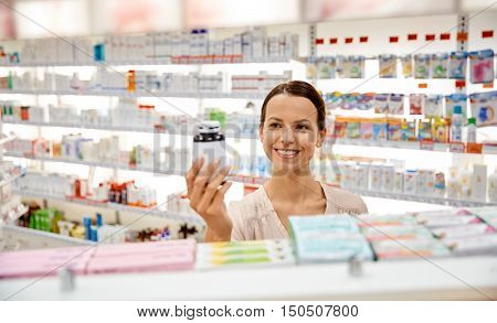 medicine, pharmaceutics, health care and people concept - happy female customer with drug jar at pharmacy