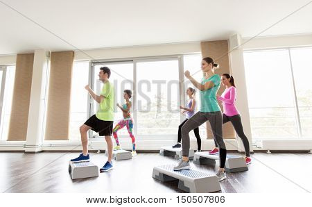 fitness, sport, exercising, aerobics and people concept - group of smiling people working out on step platforms in gym