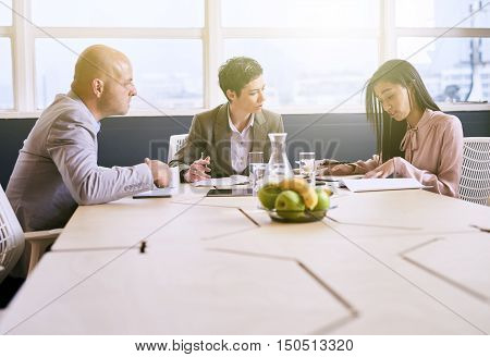 Business meeting between three executive employees, two female and one male, taking place in a birght conference table early in the morning to prepare for the week ahead.