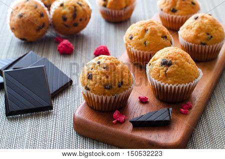 Little chocolate muffins in paper cupcake holder with crushed chocolate and dried raspberries on the wooden tray