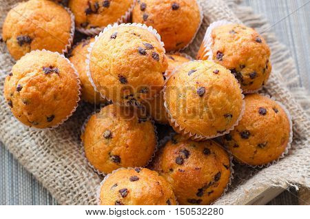 Little chocolate muffins in paper cupcake holder on the wooden tray with sacking napkin