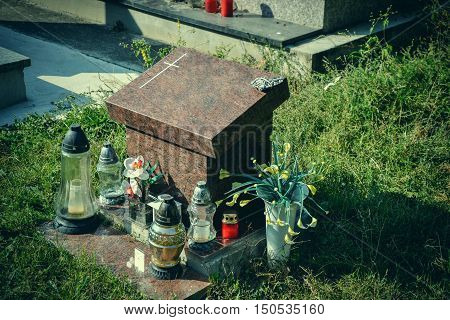 Urn grave with cross on traditional cemetery. Votive candles lantern and flowers on tomb stones in graveyard. All Saints' Day. All Souls' Day. Gravestones in village Tvrdomestice Slovakia