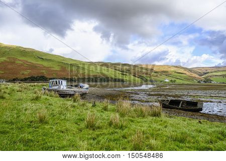 Beautiful Isle of Skye Scotland landscape. Three old abandoned wooden boat wrecks on the shore at Loch Harport