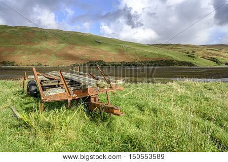 Old rusting farm trailer full of planks of timber on grass by the shore of Loch Harport Isle of Skye Scotland