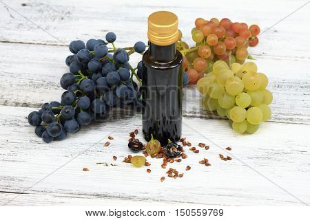 Grape seed oil and grape seeds in front fresh grapes around
