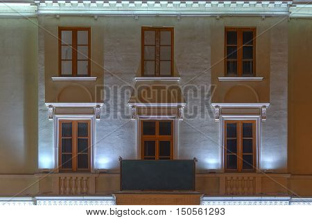 Several windows in a row and balcony on night illuminated facade of urban apartment building front view St. Petersburg Russia