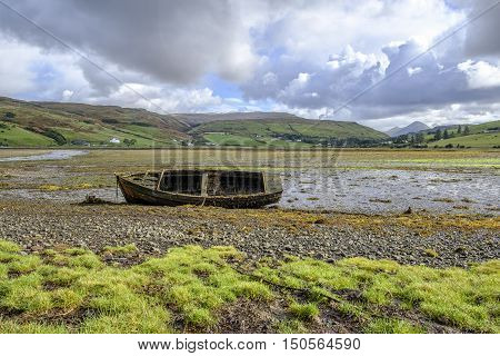 Beautiful Isle of Skye Scotland landscape. Old abandoned broken wooden row boat wreck covered in barnacles and seaweed on the shore at Loch Harport at low tide