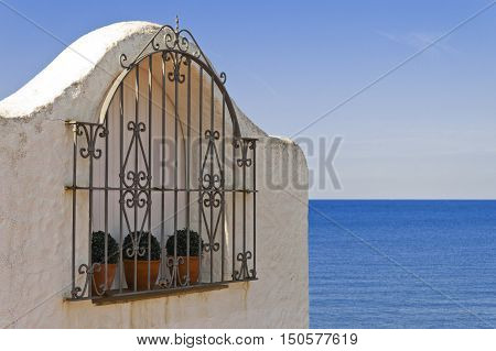 Typical spanish grated window in a white wall house Mediterranean Sea in Background. Roc de Sant Gaieta Tarragona Catalunya Spain.
