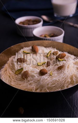 Indian sweet sutarfeni or sutar feni or firni or seviyan or laccha, shredded, flaky-rice-flour roasted in ghee, blended with melted sugar to form a cotton candy, topped with pistachio and almonds