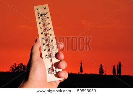 A hand and temperature scale over a red sky shows high temperatures during a heat wave.
