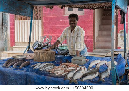 Madurai India - October 21 2013: A fish merchant displayed plenty of large fishes on blue carpet and sells them with a big smile out of his stall wheeled onto the street.