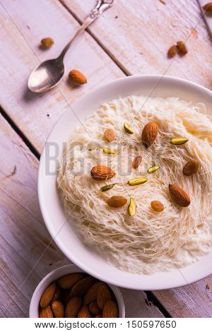 Indian sweet sutarfeni or sutar feni or firni or seviyan or laccha, shredded, flaky-rice-flour roasted in ghee, blended with melted sugar to form a cotton candy, topped with pistachio and almonds