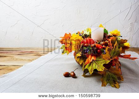 Thanksgiving centerpiece with white candle and silk fall leaves . Thanksgiving background with fall decor. Fall background. Copy space.