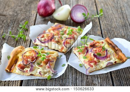 Street food: Slices of hot baked tarte flambee from Alsace with onions, bacon and sour cream served on parchment paper