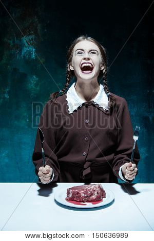 Portrait of a young girl with knife fork and and a piece of raw meat on a plate. Girl in school uniform as killer. The image in the style of Halloween and Addams family