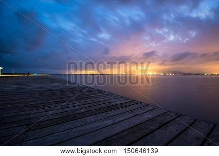 Distant city lights watched from a wooden pier.