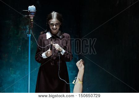 Portrait of a young girl with knife and drop counter in school uniform as killer woman against school board . The image in the style of Halloween and Addams family
