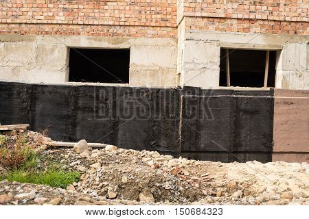 Construction techniques for waterproofing basement and foundations. Insulation material on the basement concrete wall. Waterproofing house foundation with spray on tar and roll waterproofing