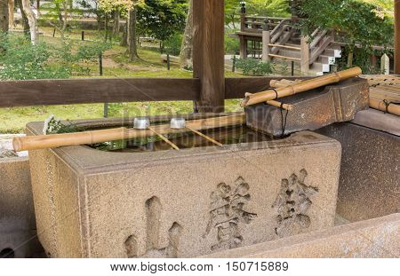 Kyoto Japan - September 15 2016: At the Shinnyo-do Buddhist Temple the large stone Harai hand wash basin offers two cups on a stick. The rinsing is called Temizu. Set in park.