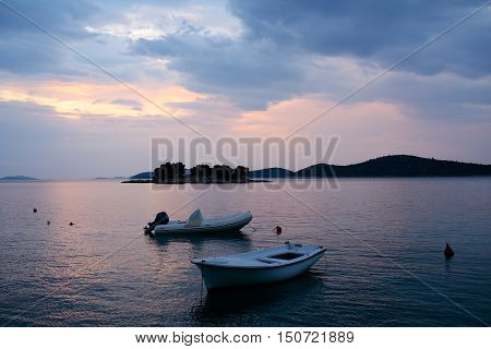 White rowboat and rubber boat with motor at anchor in calm blue sea water inshore after sunset on beautiful evening seascape