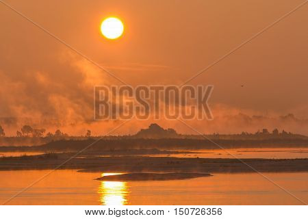 Bright autumn sunrise on the banks of the river Volga. The wind scatters the morning mist.