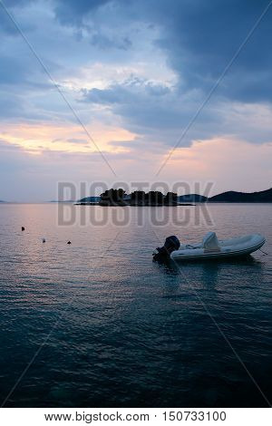 White boat inflatable rubber vessel with motor at anchor in calm blue sea water inshore after sunset on beautiful evening seascape