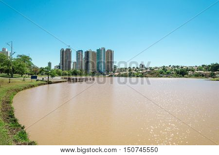 Lakeshore on the left with grass and some trees. Water lake and background city buildings on a sunny day.
