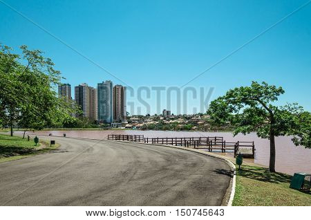 Walking trail, green trees, an observation deck over lake water, buildings and a blue sky background in a park.Beautiful day to relax and do some exercises. To escape the hard life of the city.
