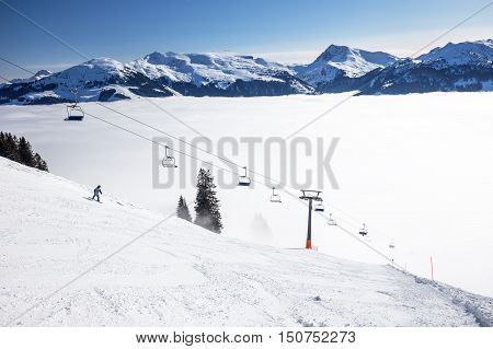 Skiers On Ski Lift Enjoying The View To Foggy Alps In Austria And Beautiful Snowy Country Panorama I