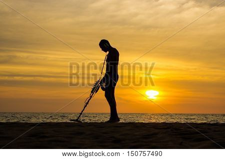 a treasure hunter with Metal detector on sunset on the beach