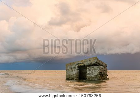 Ruins in the sea with storm clouds and dramatic sunset sky.