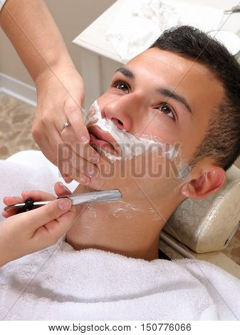 Shaving at the barber of a young boy in retro style with razor and shaving soap