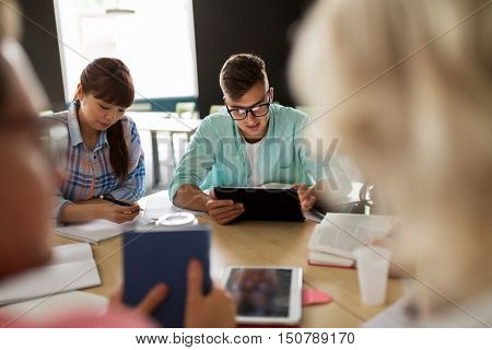 education, high school, learning, people and technology concept - group of international students sitting at table with tablet pc computers, books and notebooks at university