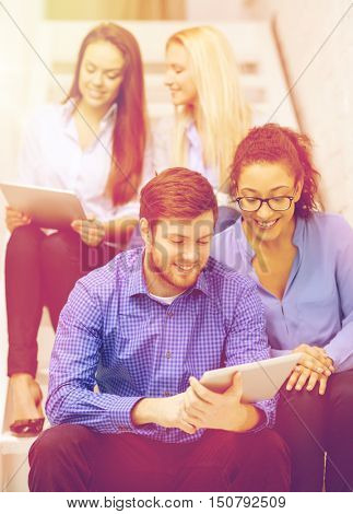 business, technology and startup concept - smiling creative team with tablet pc computer sitting on staircase