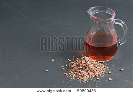 glass jug with infusion of oak bark with a dry shredded oak bark at blackboard