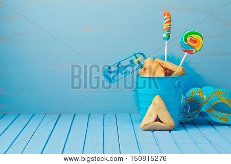Purim traditional gifts with hamantaschen cookies noisemaker and carnival mask on blue background